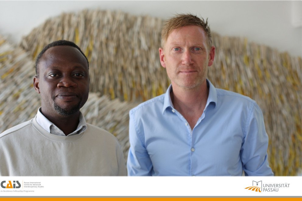 PICAIS-Fellow Dr. Edward Asiedu neben seinem Host Prof. Michael Grimm. Darunter das Logo des PICAIS und der Universität Passau.